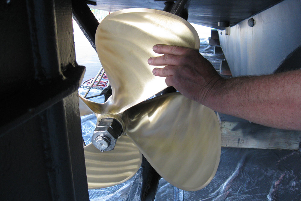 Stand between the propellers facing the bow and reach out to the closest upper blade of each propeller.